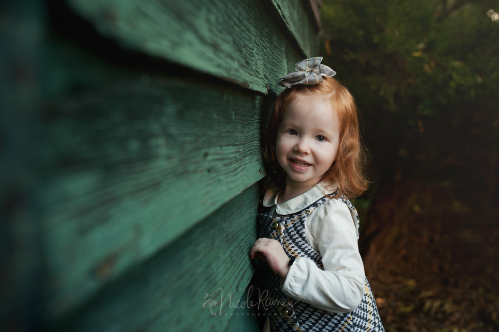 Smiling red headed little girl by green wall